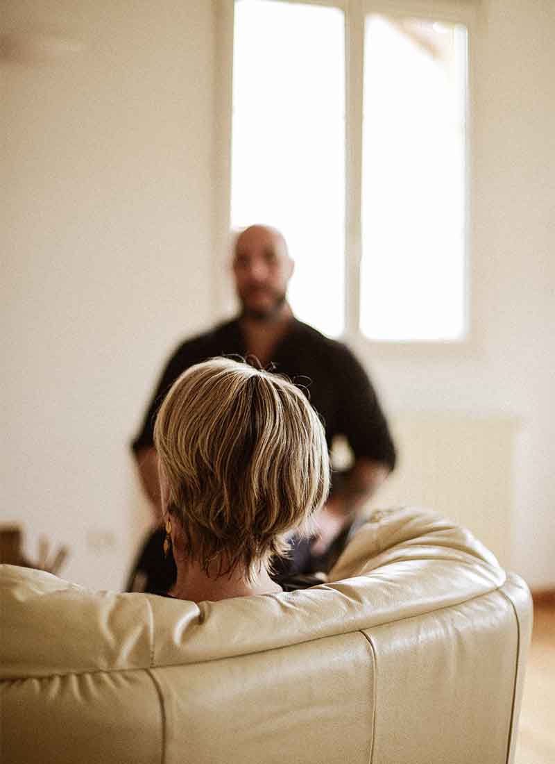 DSC_6188 femme de dos assise sur un canapé en cuir beige qui écoute un homme en arriere plan