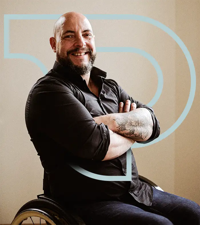 steewe-lefay-pulse-consult homme d'une quarantaine d'année chauve et barbu, souriant. Il est en chemise noire et croise ses bras tatoués. Il est en chaise roulante