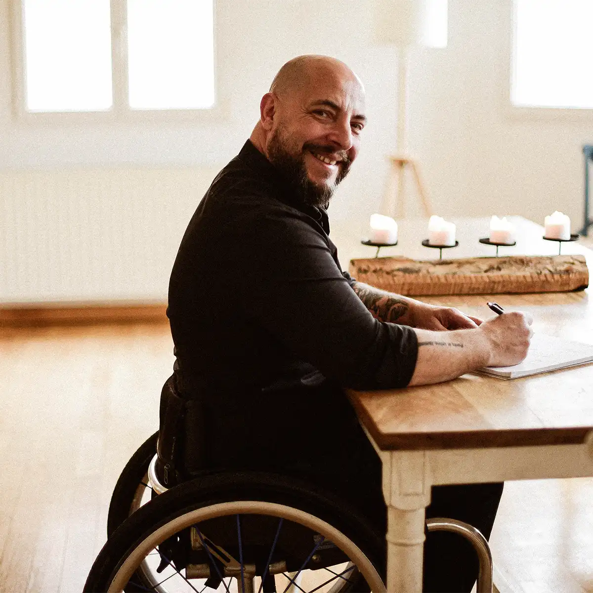 steewe homme de 40 ans chauve, barbu et souriant. Il est assis sur sa chaise roulante à table, l'ambiance est très chaleureuse<br />