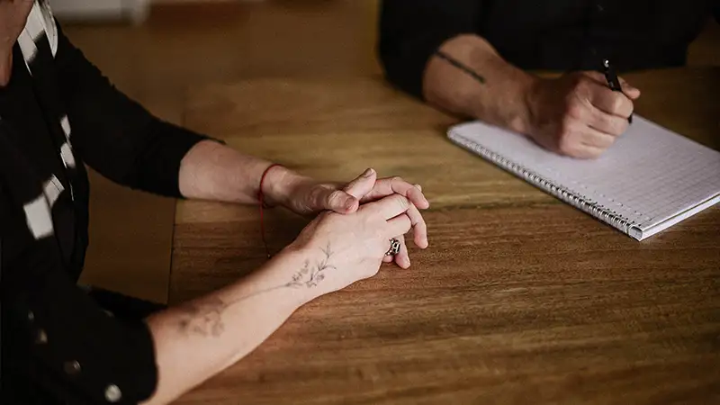 homme tatoué prend des notes sur un cahier pendant que sa patiente a les mains jointes mais détendues